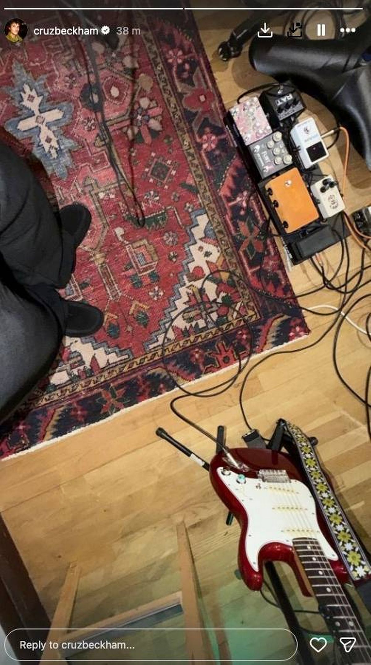 An individual, clad in dark attire, is seated on a wooden floor adorned with an intricate oriental rug. Various electronic devices and cables are meticulously arranged on the rug.