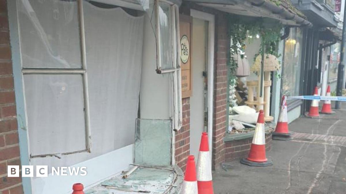 A shop front with a broken window.  Another window pane is cracked and damaged.  Scaffolding is on the pavement in the corner of the picture. The photo was taken in the dark.