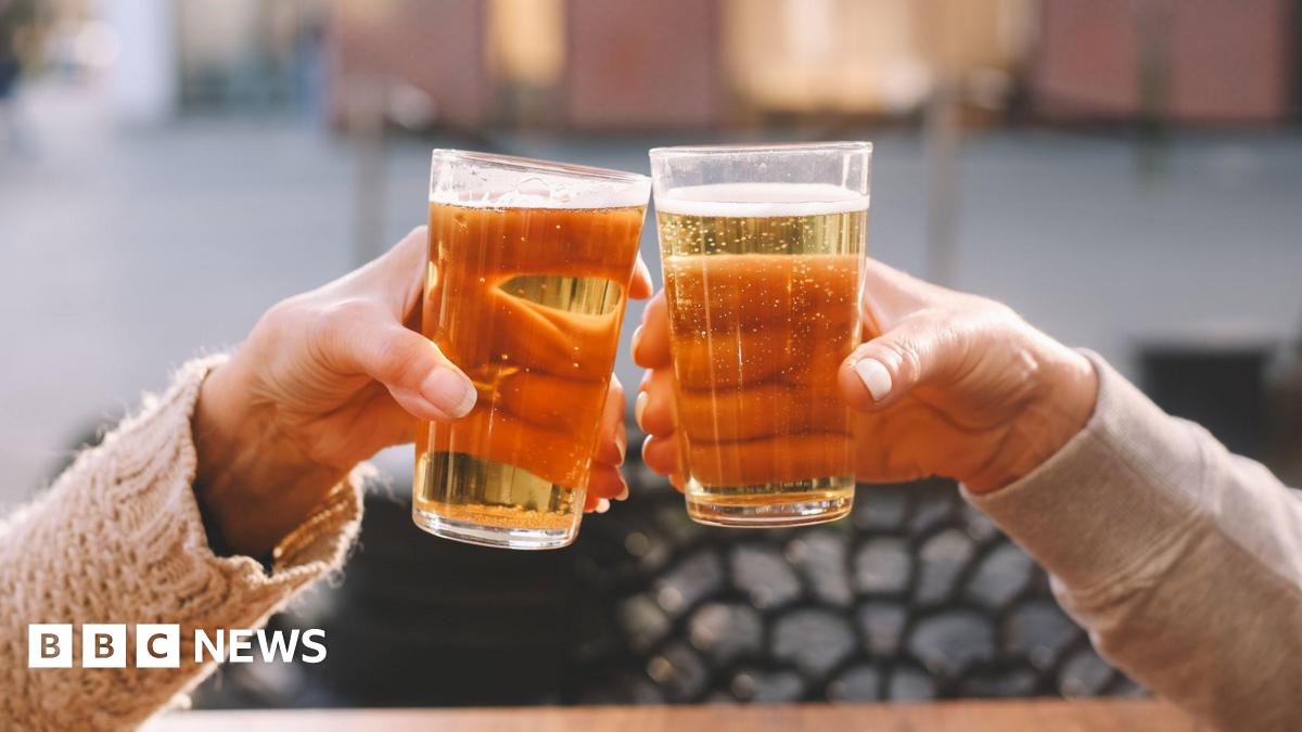 A stock photo of two hands both holding pints of lager as they cheers their glasses.