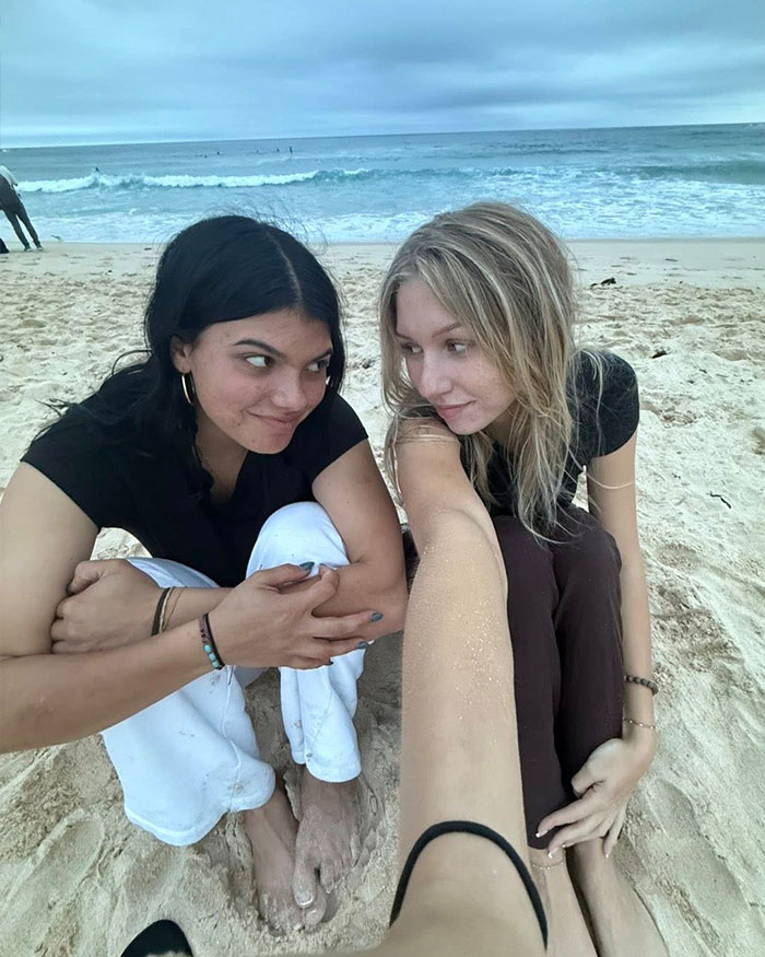 Two young women sitting on a sandy beach near the ocean, related to autopsy results uncovering startling clues.