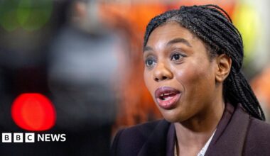 Kemi Badenoch, wearing a brown suit jacket and against a blurred background, speaks during an engagement