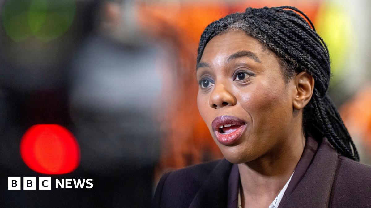 Kemi Badenoch, wearing a brown suit jacket and against a blurred background, speaks during an engagement