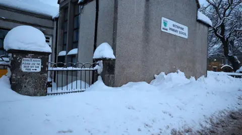 Getty Images A school building with snow piled up outside it. On the wall there is a sign which reads 'Botriphine Primary School'.