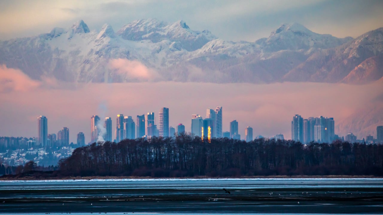 tall sky scrapers stand below large snow capped mountains.