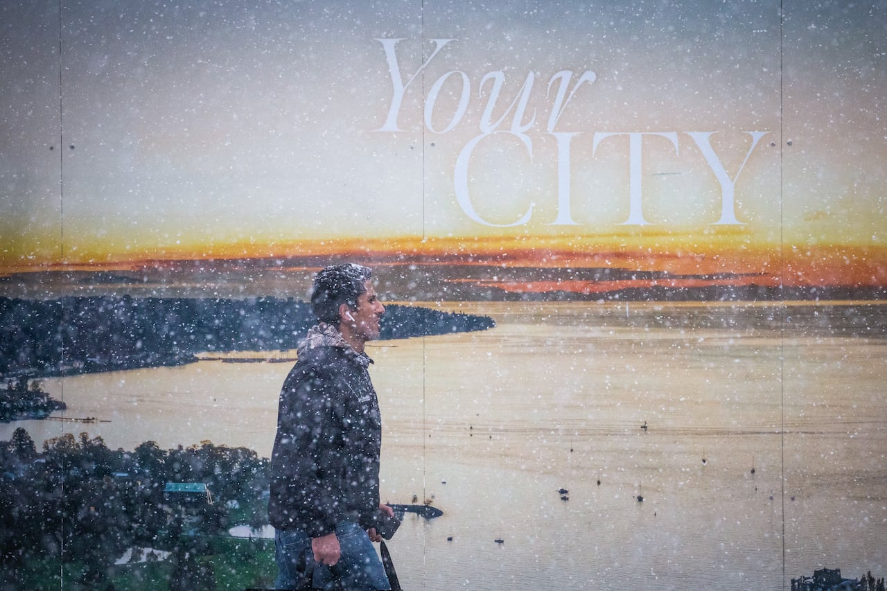 A man walks past a billboard with a picture of sunset while snowing.