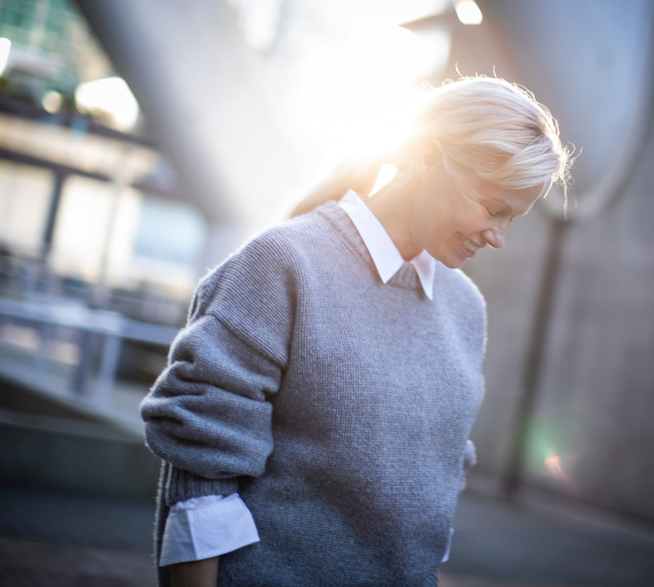 A woman with blonde hair smiles as she walks down a sidewalk on a sunny day.