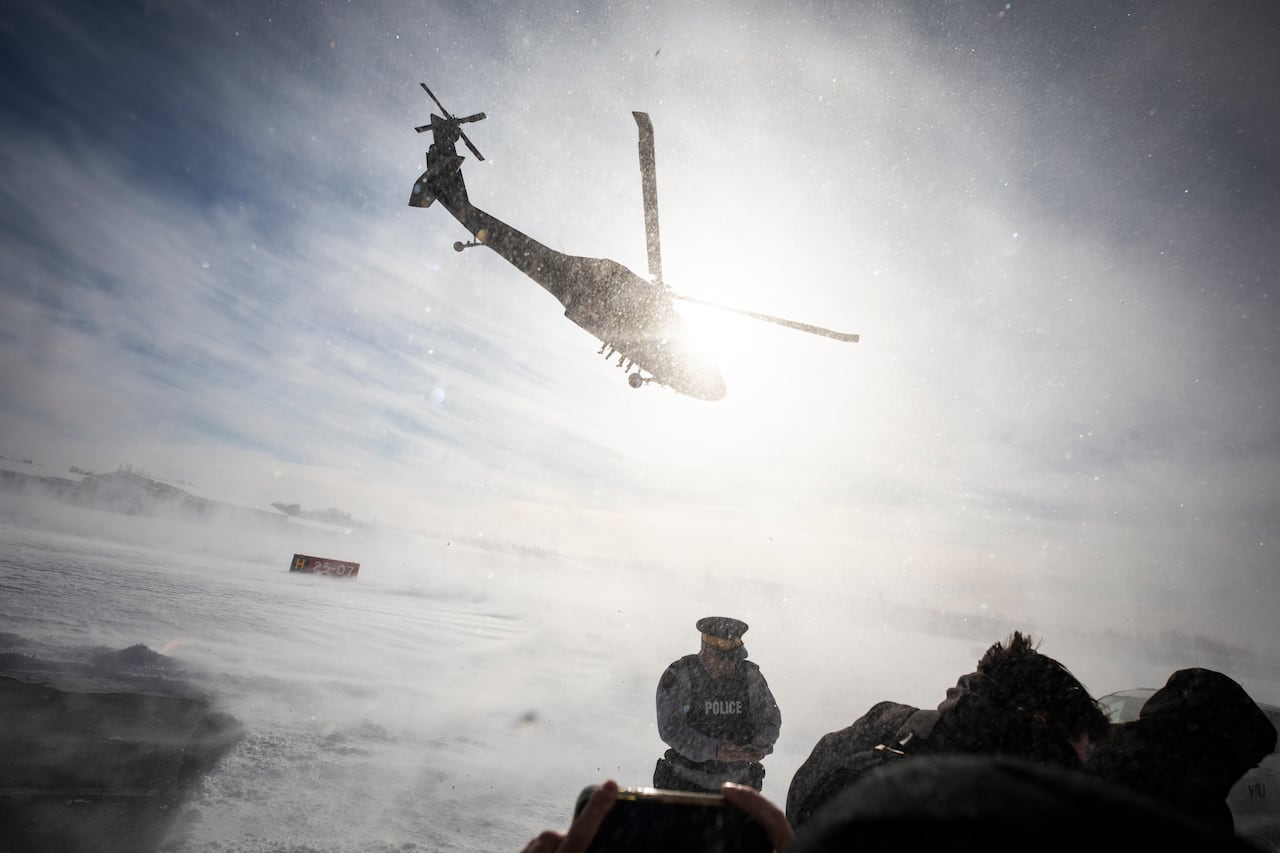 A helicopter takes off close to a group of people during a snowstorm.