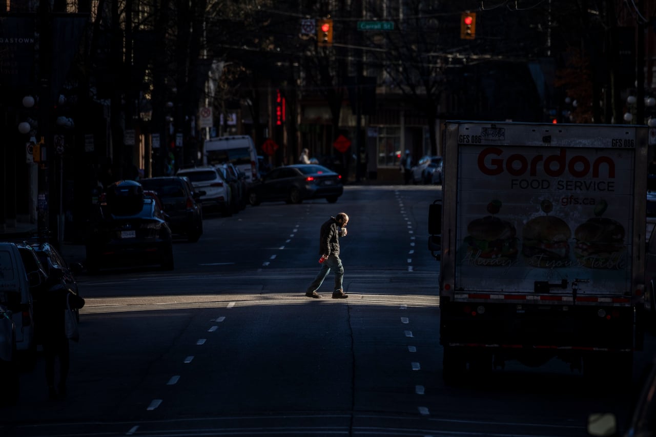 A person walks across a street in a beam of sunlight.