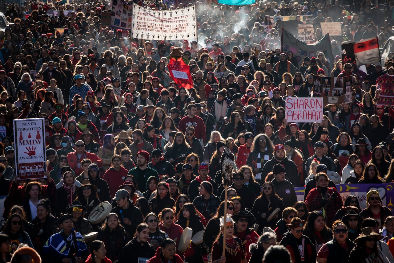 A large group of people walk down a street as the sun shines on their backs.