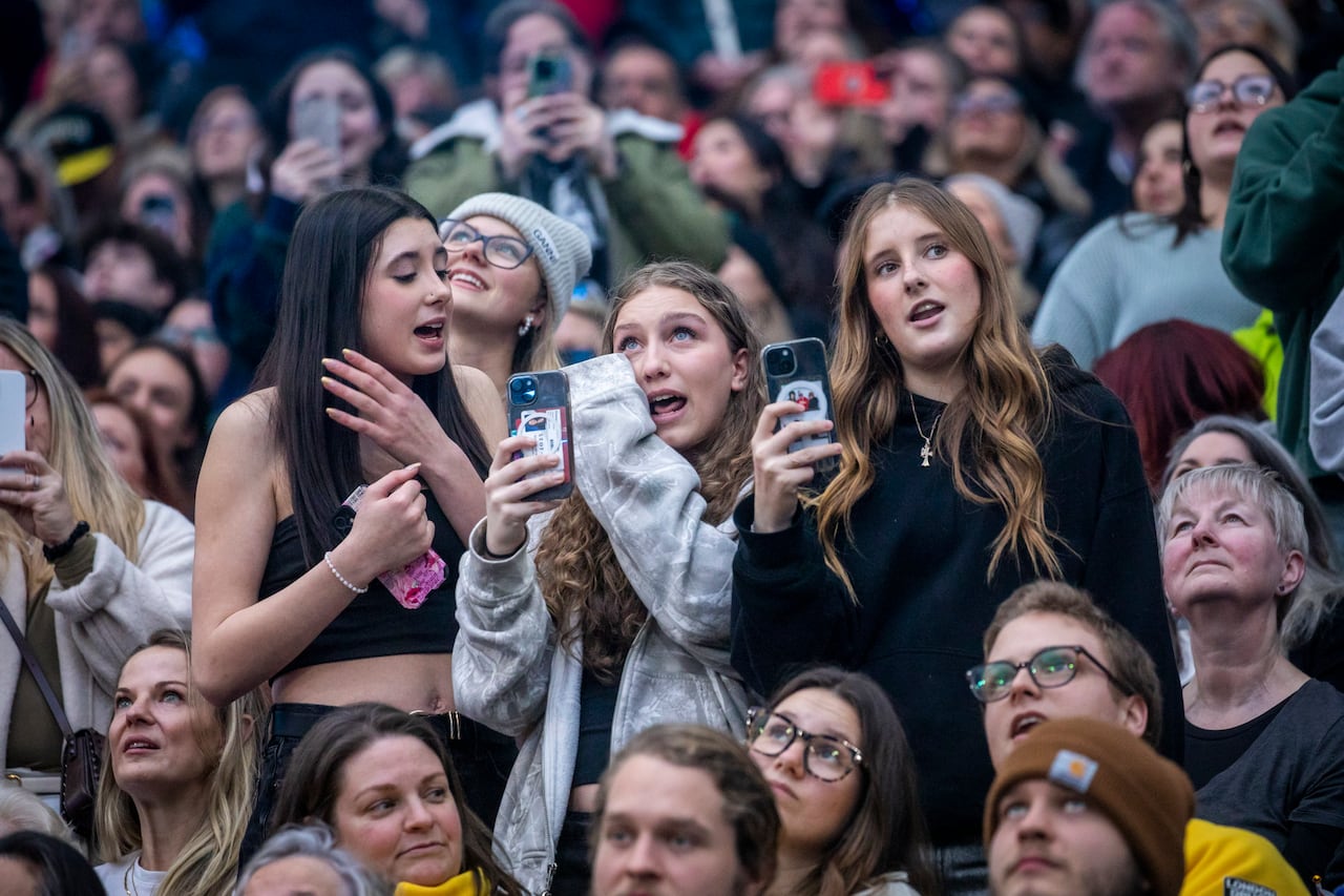 A group of teenage girls hold their cellphones as they stand in a group.