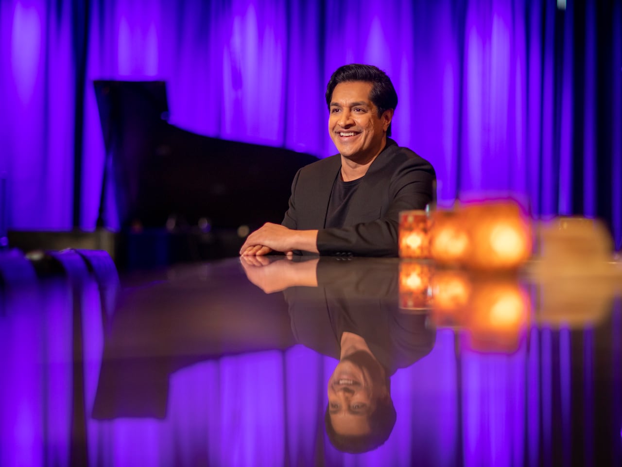 A man sits at a bar with his reflection and candles.