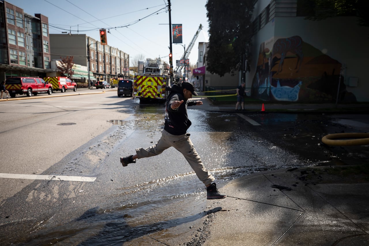 A man jumps over a stream of water flowing down a street.