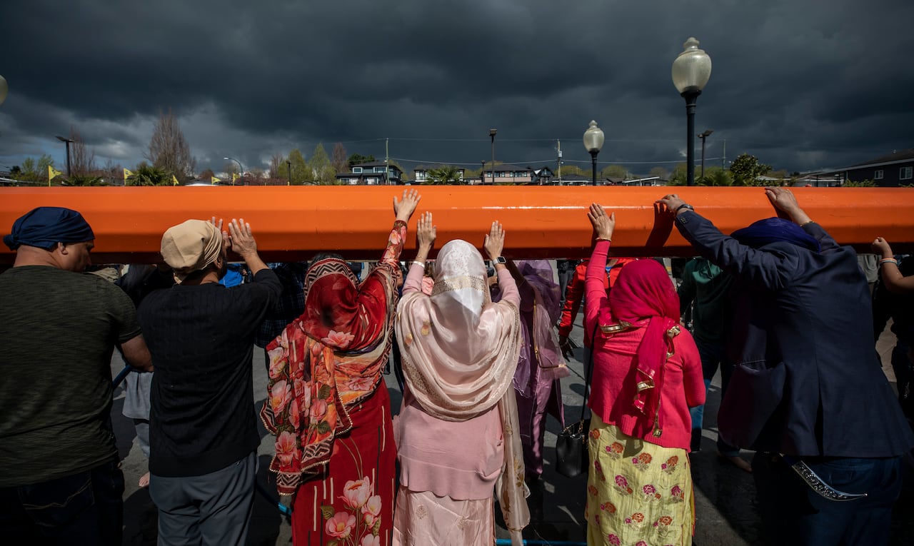 A group of people wearing headscarves touch a large orange pole.