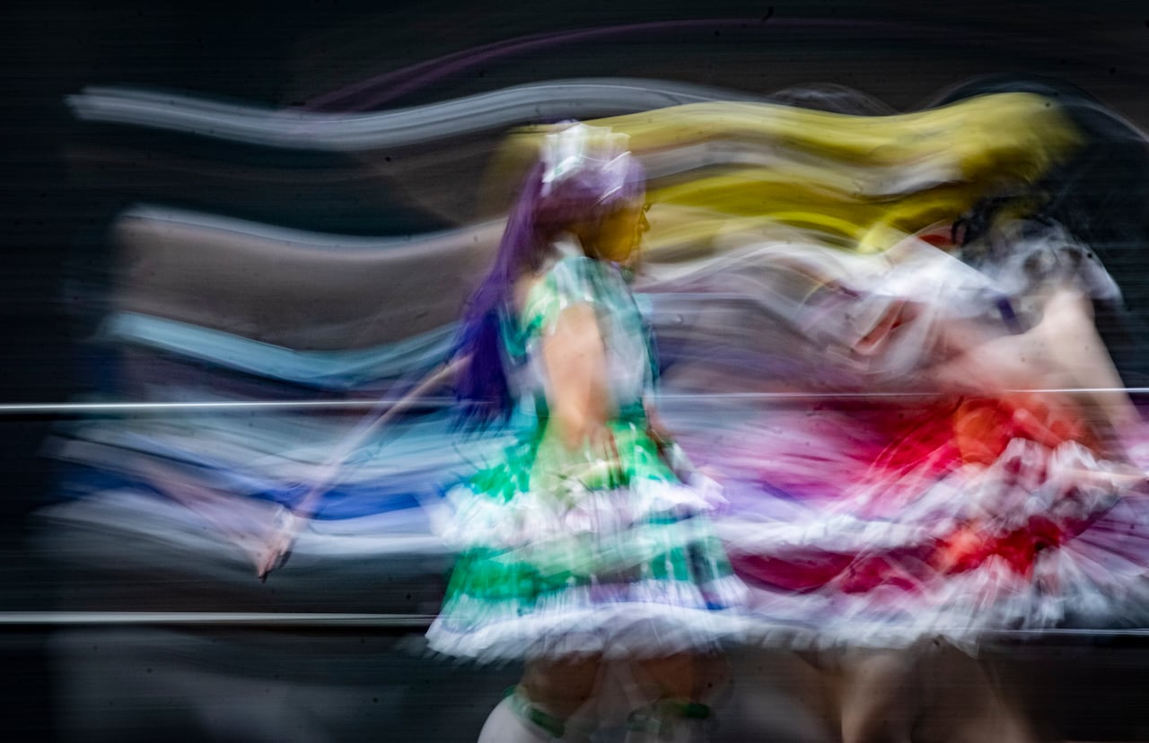 A woman in a brightly covered costume dances across a stage.