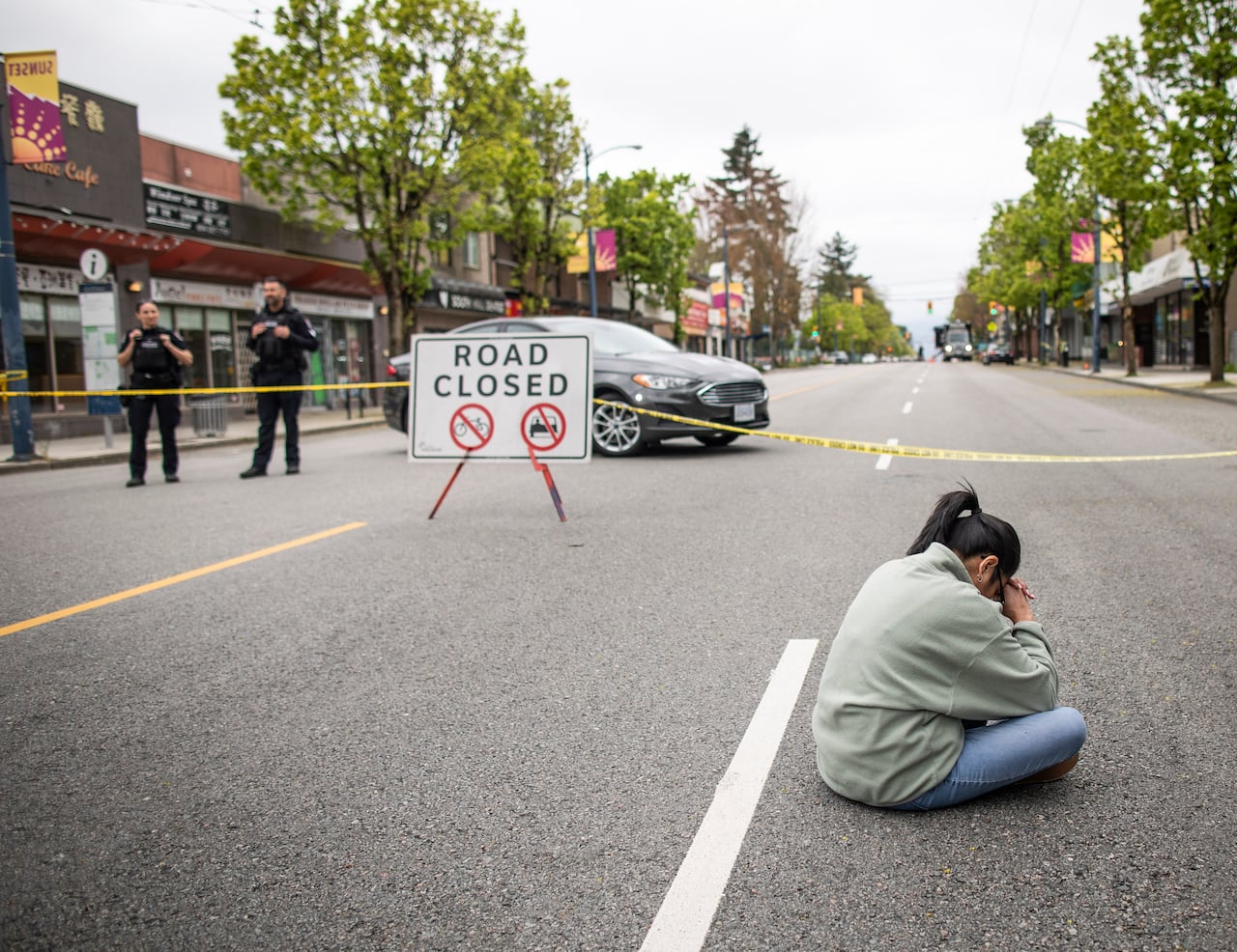 A woman sits on an empty street with police tape nearby.