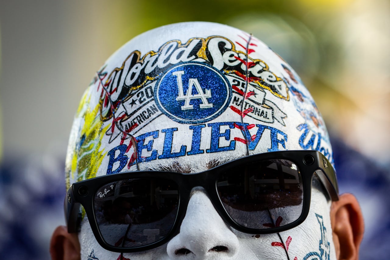 A man with his head fully covered in baseball related makeup wears sunglasses during a picture.