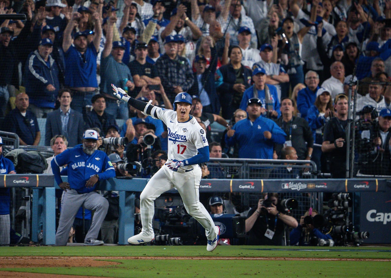 A baseball player wearing a white and blue uniform throws his bat in the air while running.