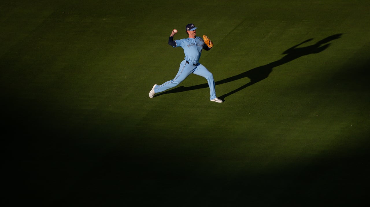 A baseball player wearing a blue jersey throws a ball as the sun sets on the field.