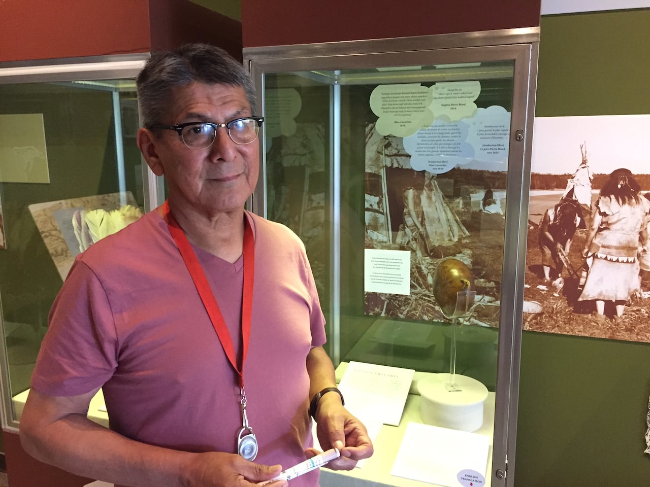 A man in a t-shirt stand in front of a Mi'kmaw museum exhibit.