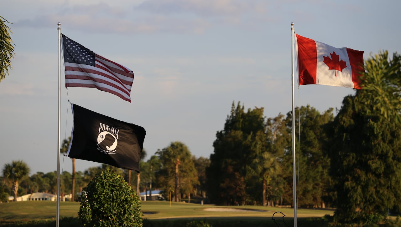 Two flags fly against a backdrop of a golf course.