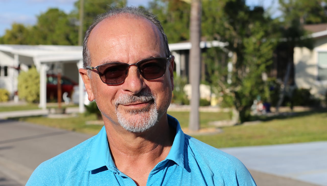 A man in a blue shirt and sunglasses stands beside a street.