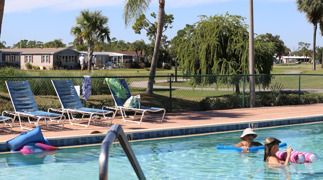Two people enjoy the water in a swimming pool as a golfer walks the course behind them.