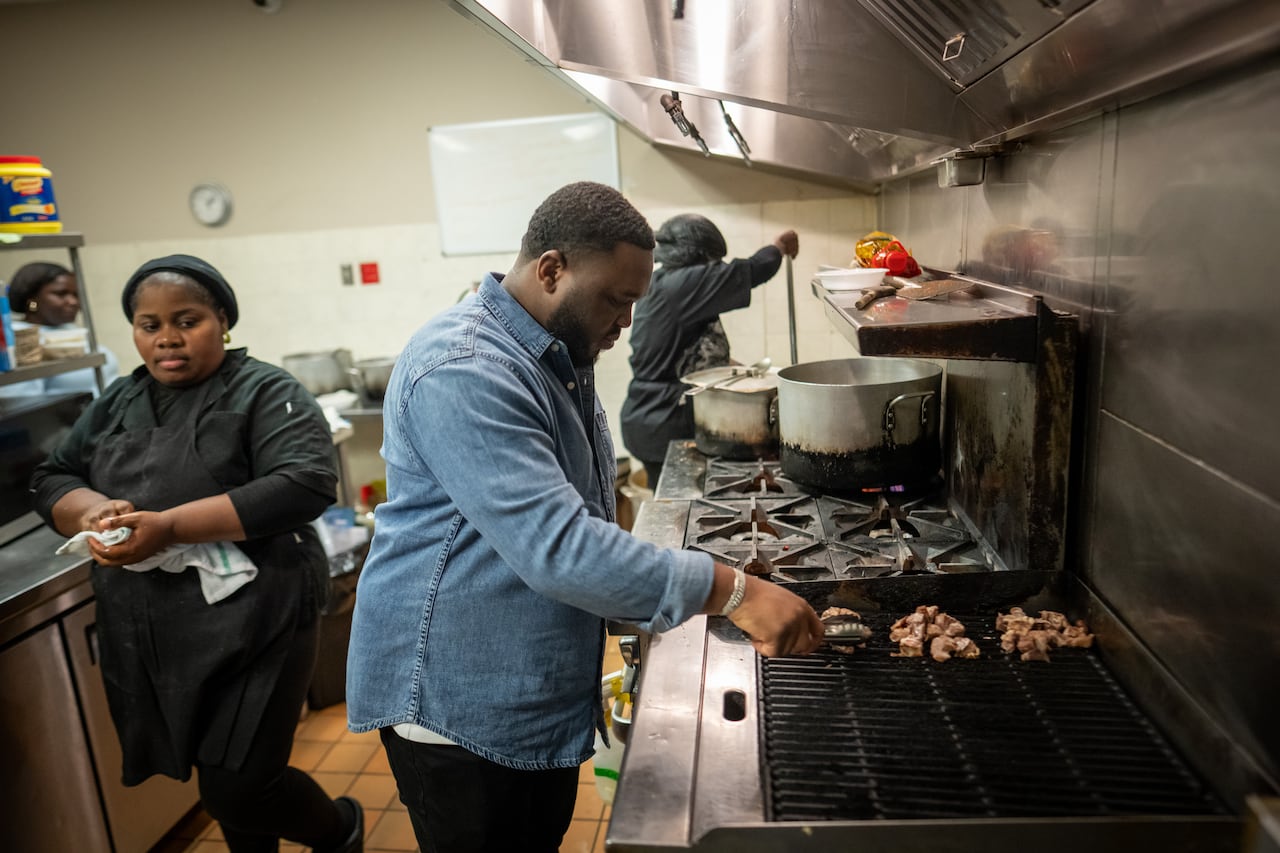 A man wearing a denim shirt stands at a commercial grill
