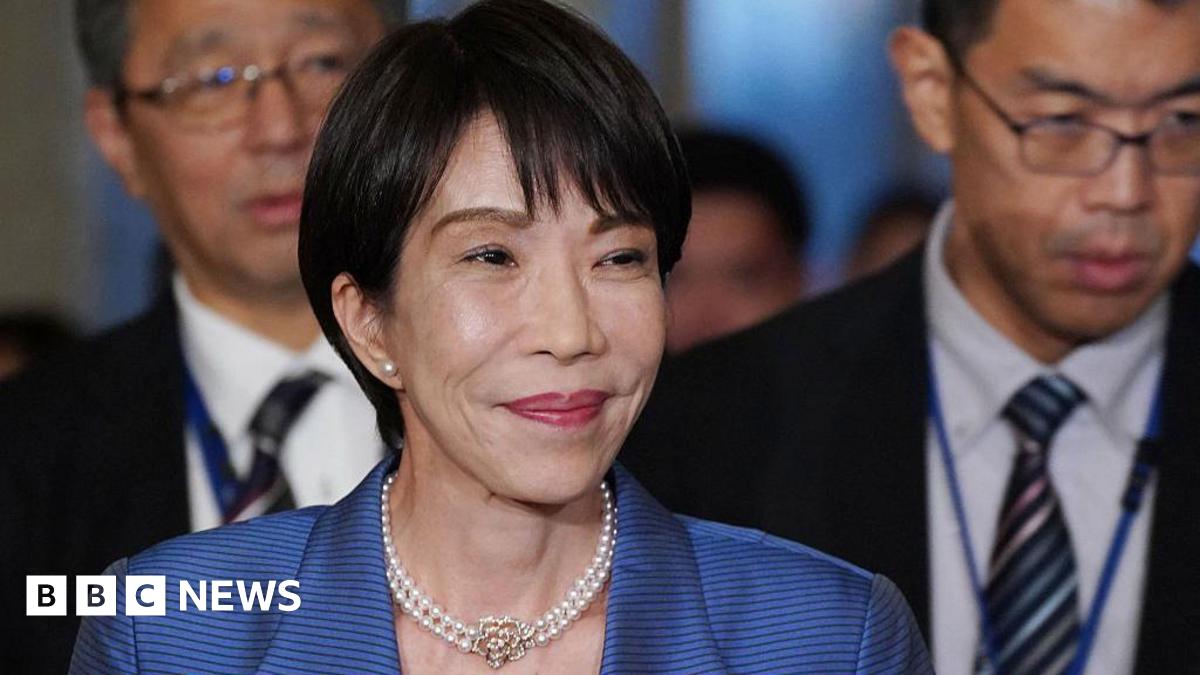 Japan's Prime Minister Sanae Takaichi, in a pearl necklace and blue striped blazer, smiles as she arrives for a debate with opposition party leaders in the parliament building on November 26, 2025