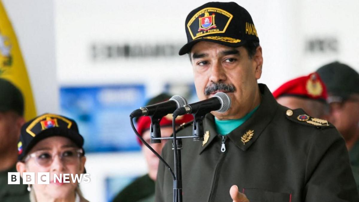 Venezuela’s leader Nicolas Maduro, wearing a military uniform, stands in front of two microphones as he attends a year-end salutation to military forces his wife Cilia Flores.