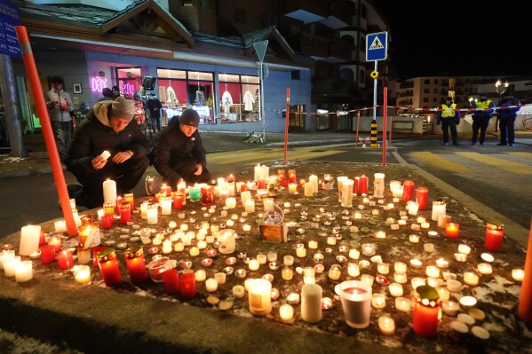 People lay candles near the Le Constellation bar, where a devastating fire left dead and injured during the New Year's celebrations in Crans-Montana, Swiss Alps, Switzerland, Thursday, Jan. 1, 2026. (AP Photo/ Antonio Calanni)