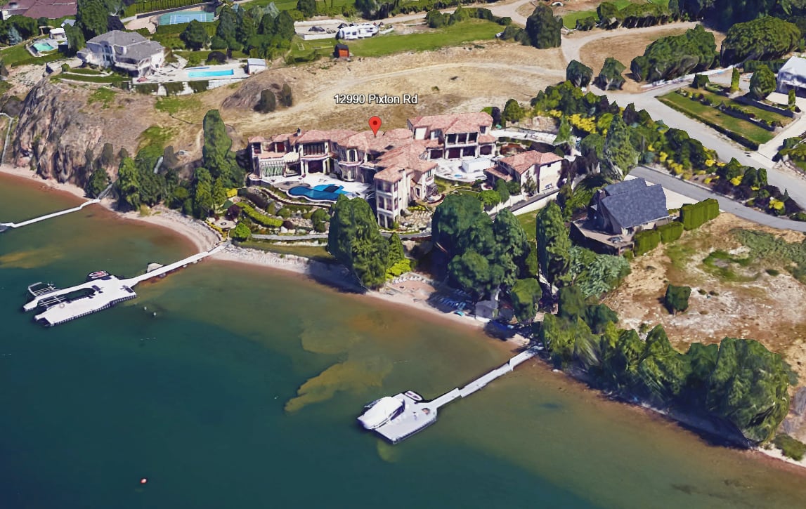 An aerial view of a waterfront mansion with a pool and dock coming off the shore