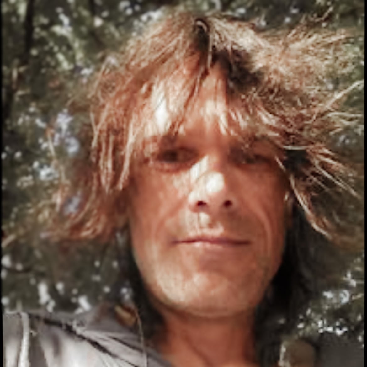 A man with long hair looks at the camera.