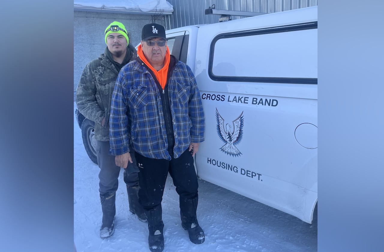 Man in blue checkered jacket and black baseball cap stands next to a man with a camouflage jacket and bright yellow winter hat in the snow