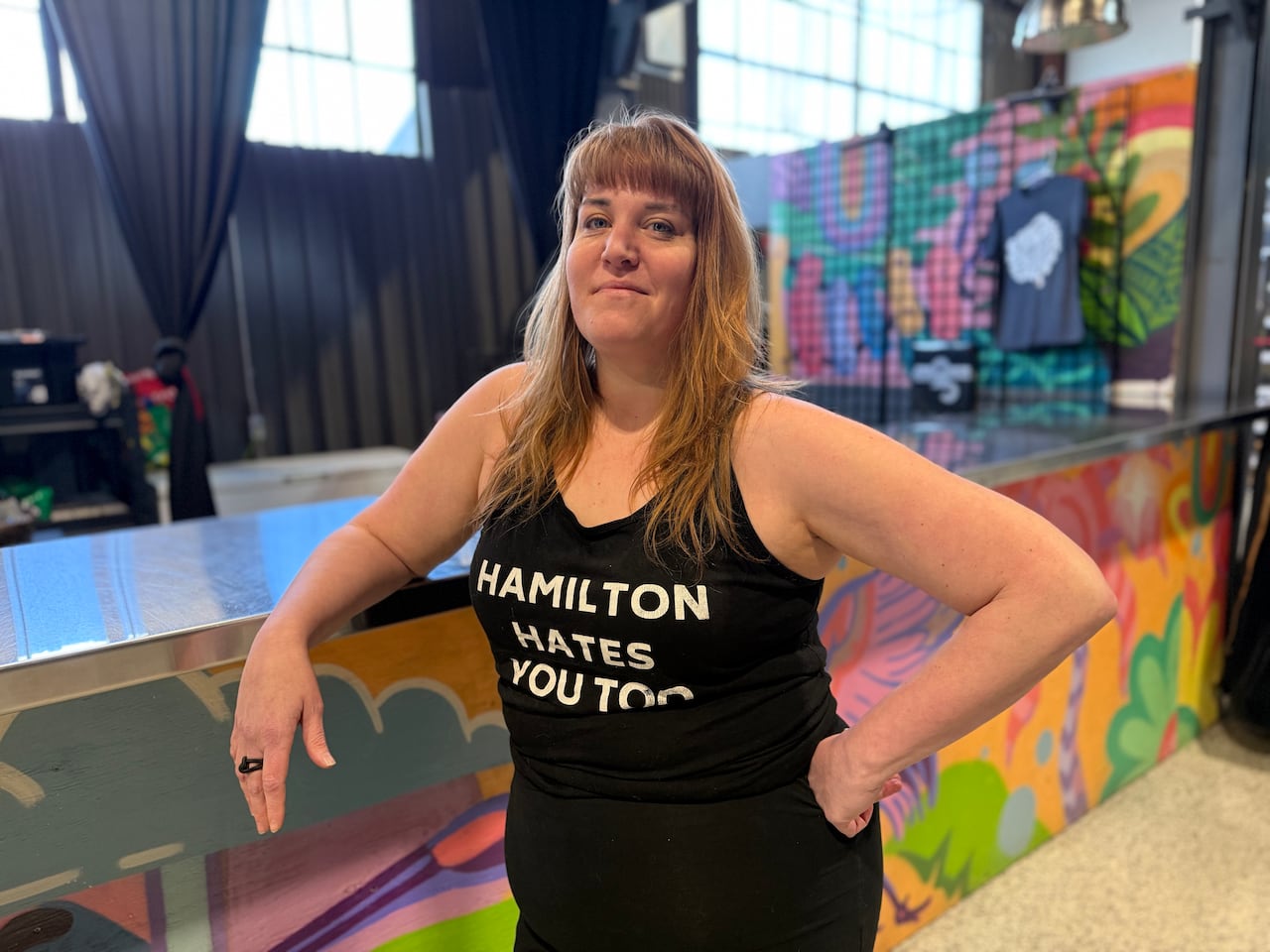 Woman stands at colourful bar with a shirt that says "Hamilton hates you too"