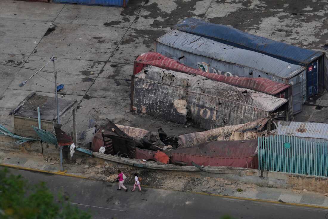 Pedestrians walk past destroyed containers lay at La Guaira port 