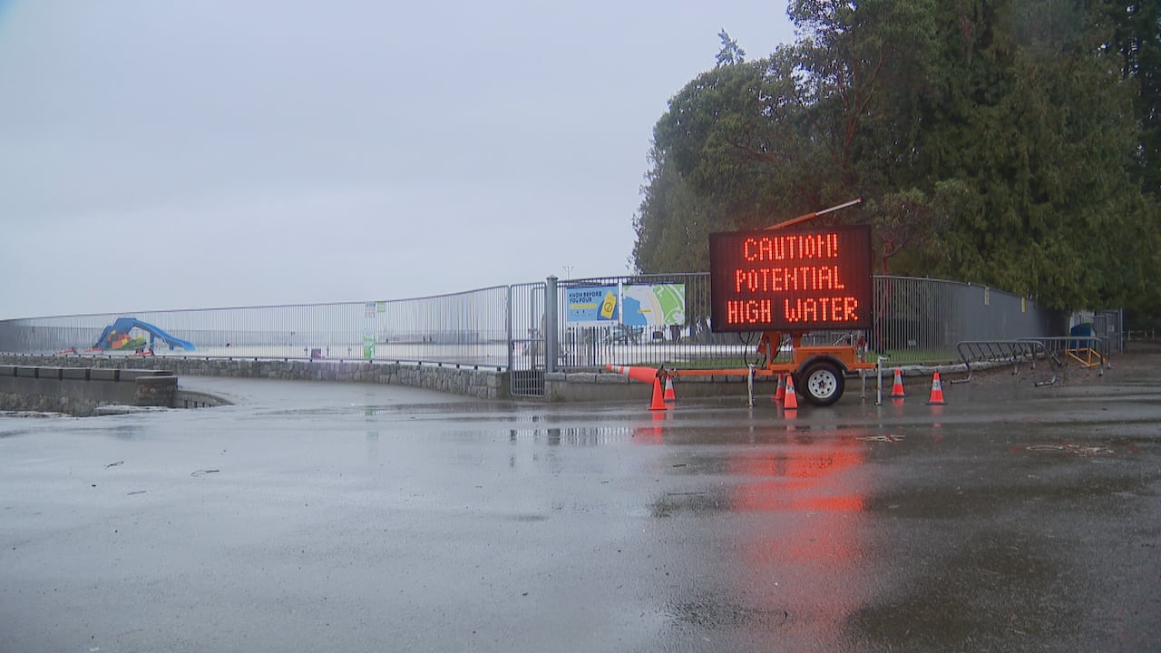 A light-up sign reads 'Caution! Potential high water' in front of an outdoor pool on Vancouver's Seawall