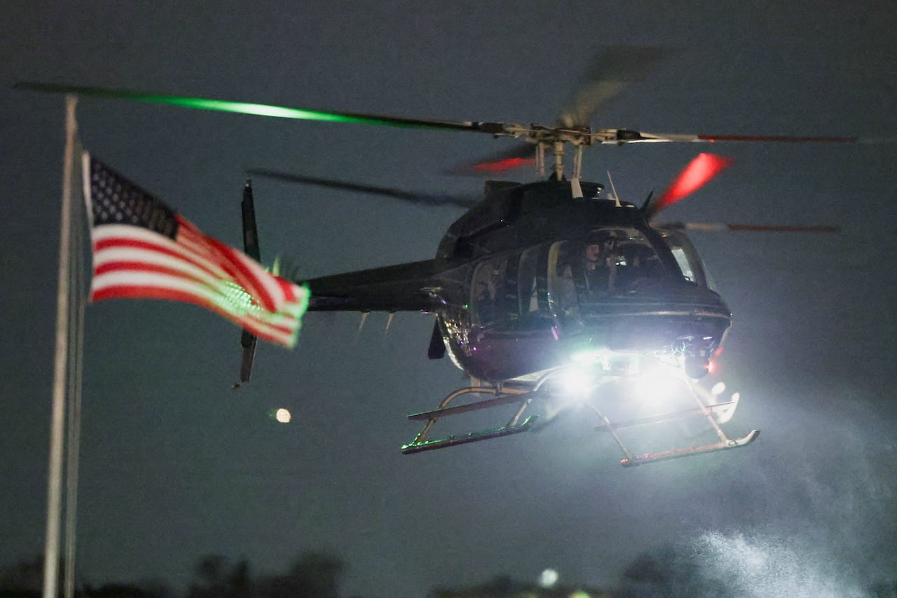 A helicopter lands at night near an American flag.