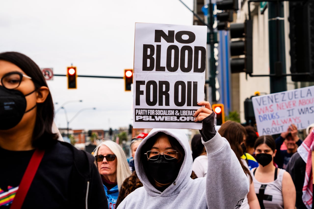 A woman wearing a face-covering holds up a sign that says "No blood for oil."