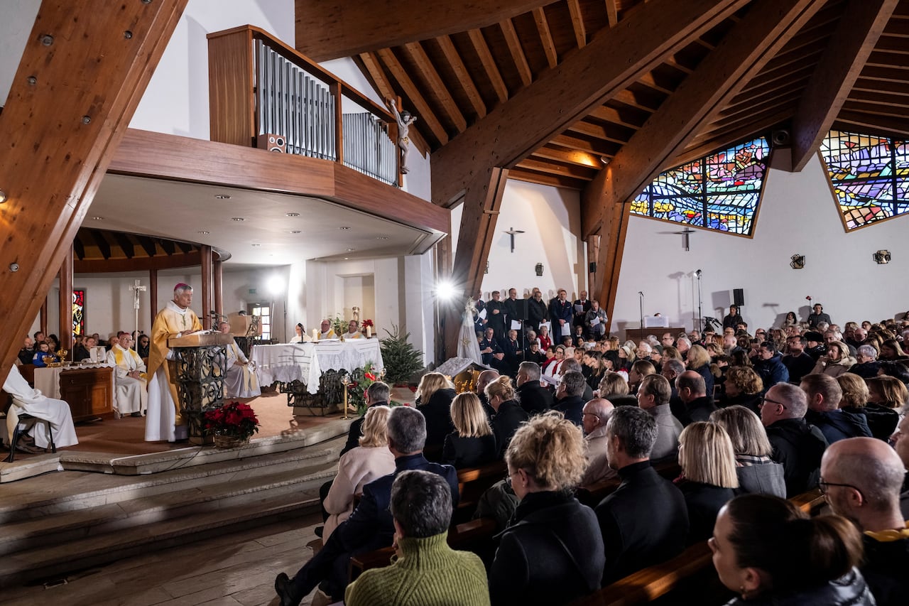 A bishop in white and yellow dress speaks to a large crowd seated in a church.