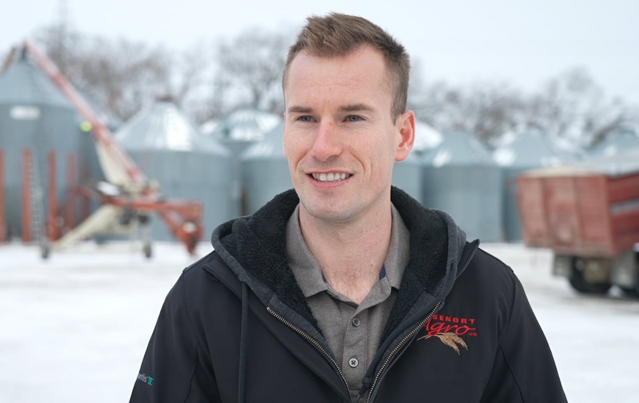 A man smiles with grain bins in the background
