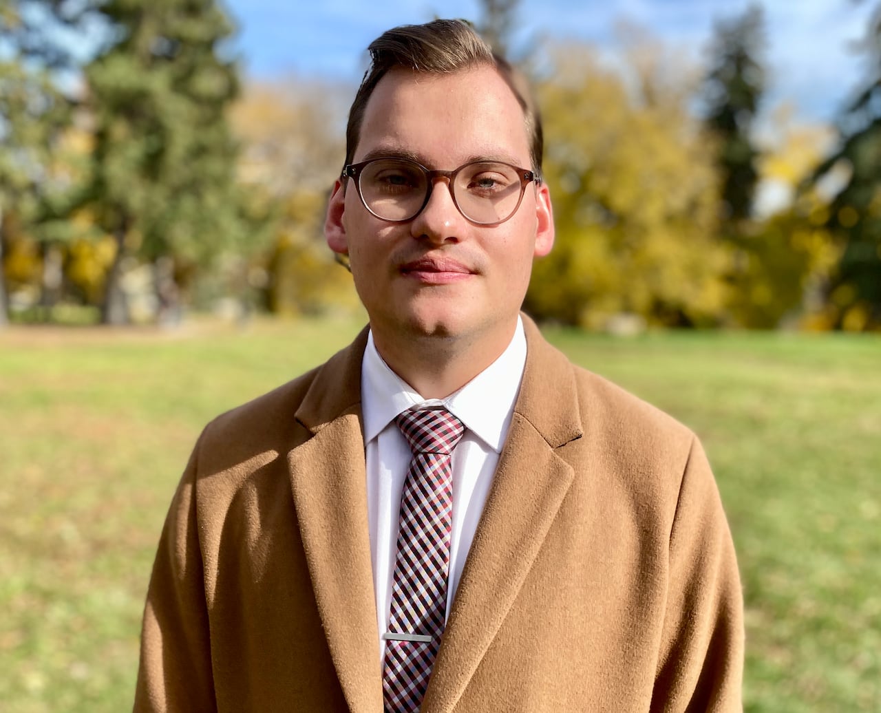 A man in a tan jacket, white shirt and tie. 
