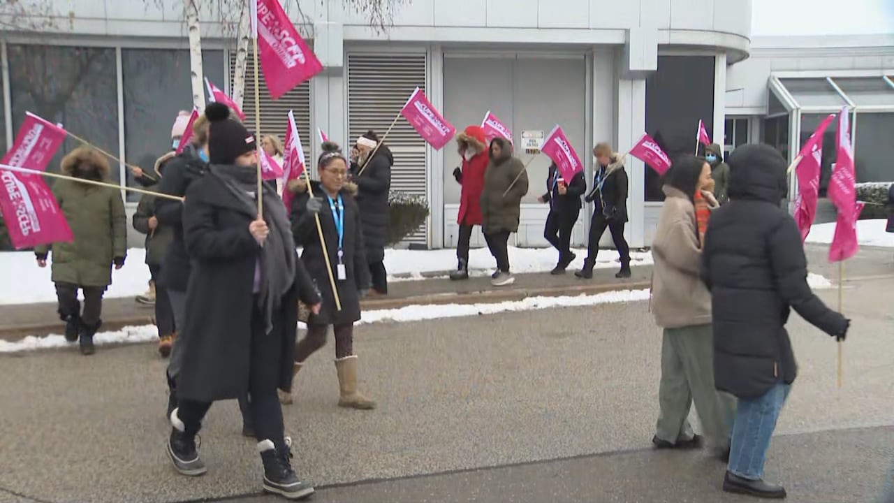 Workers march holding pink flags.