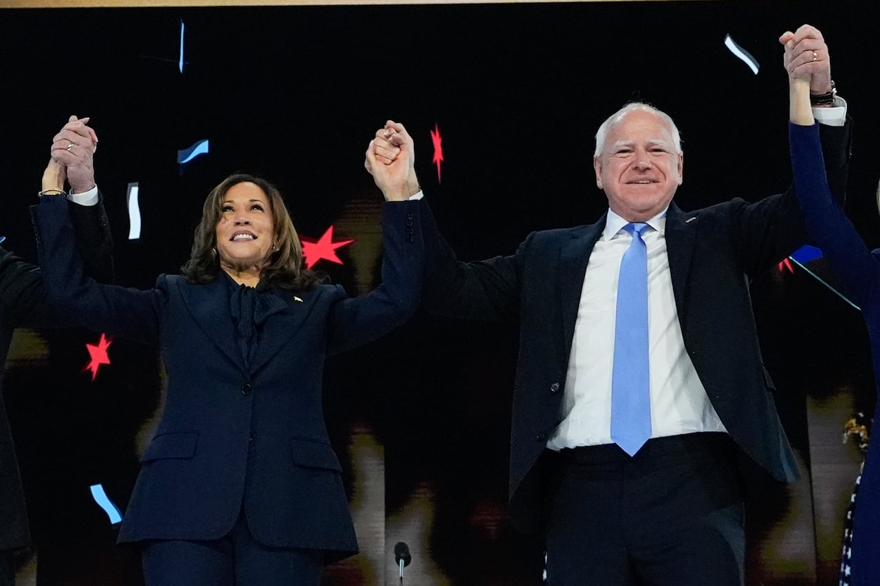 A man and a woman in suits lift arms with one another on a stage. 
