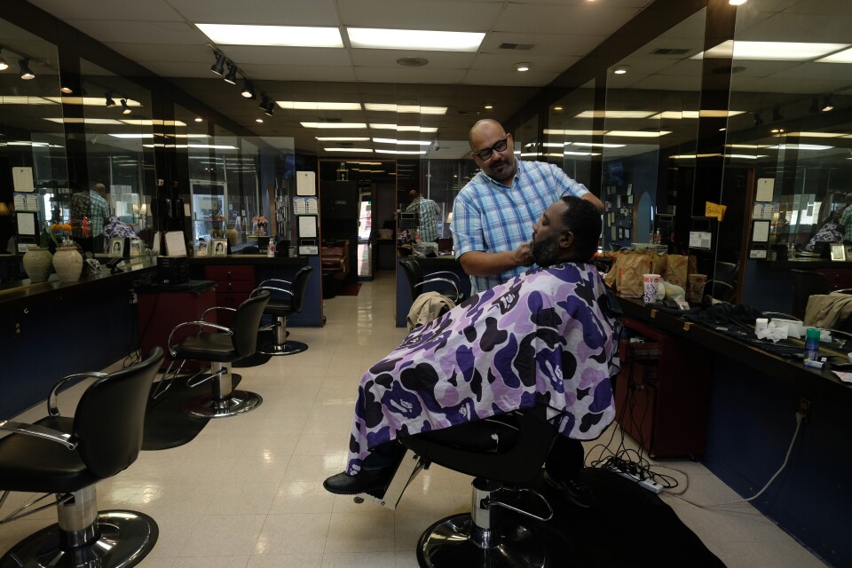 A barber tends to a customer in a mostly empty salon.