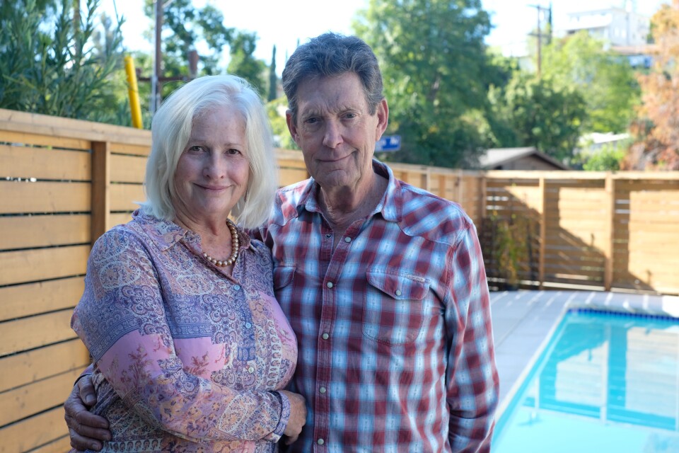 A white woman with light hair and a white man with gray hair stand near a pool.