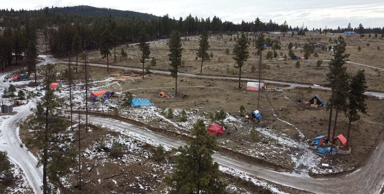 Overhead visuals of a grassy area with a few tents and debris visible.
