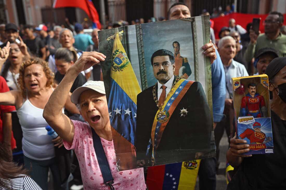 A woman standing among a crowd of people holds up a portrait of ousted Venezuelan President Nicolás Maduro in Caracas, Venezuela, on Saturday after he was captured by U.S. forces.