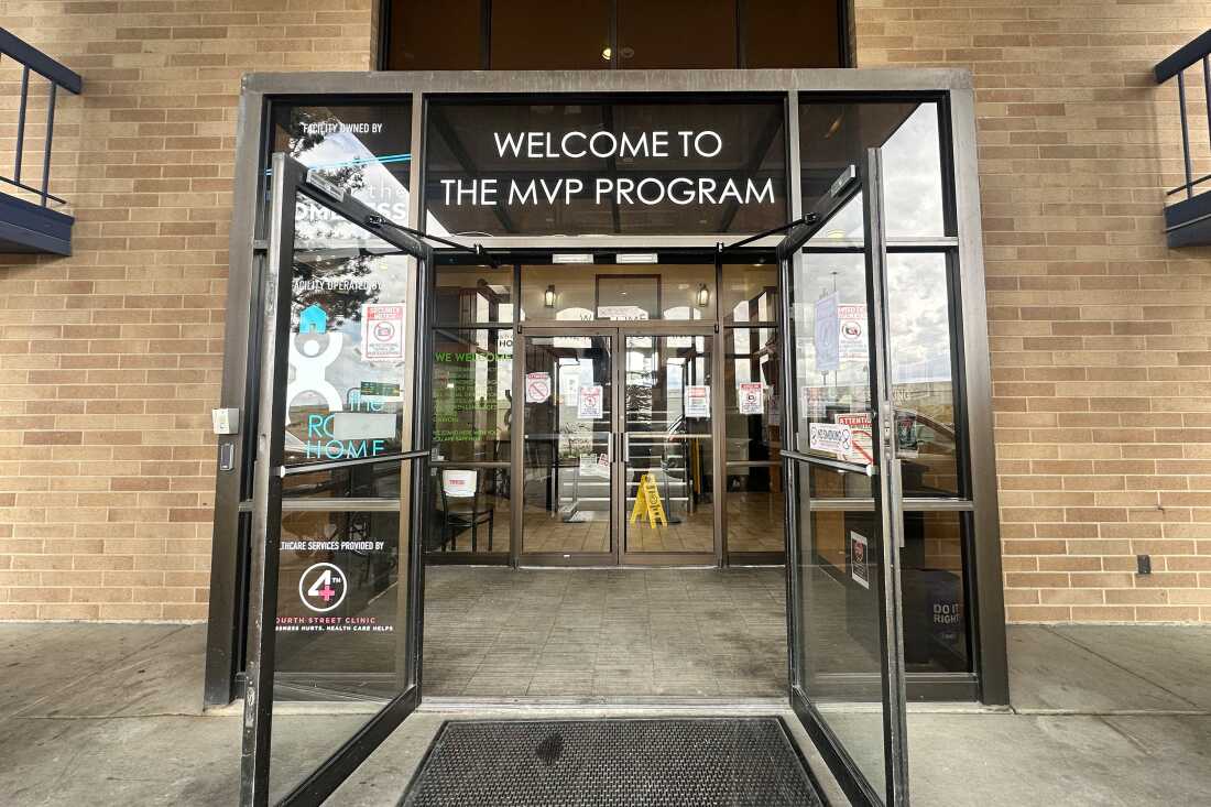 This photo shows the double glass doors of the Medically Vulnerable People shelter in Sandy, Utah. The building's exterior walls are brown bricks. Above the glass doors are the words "WELCOME TO THE MVP PROGRAM."