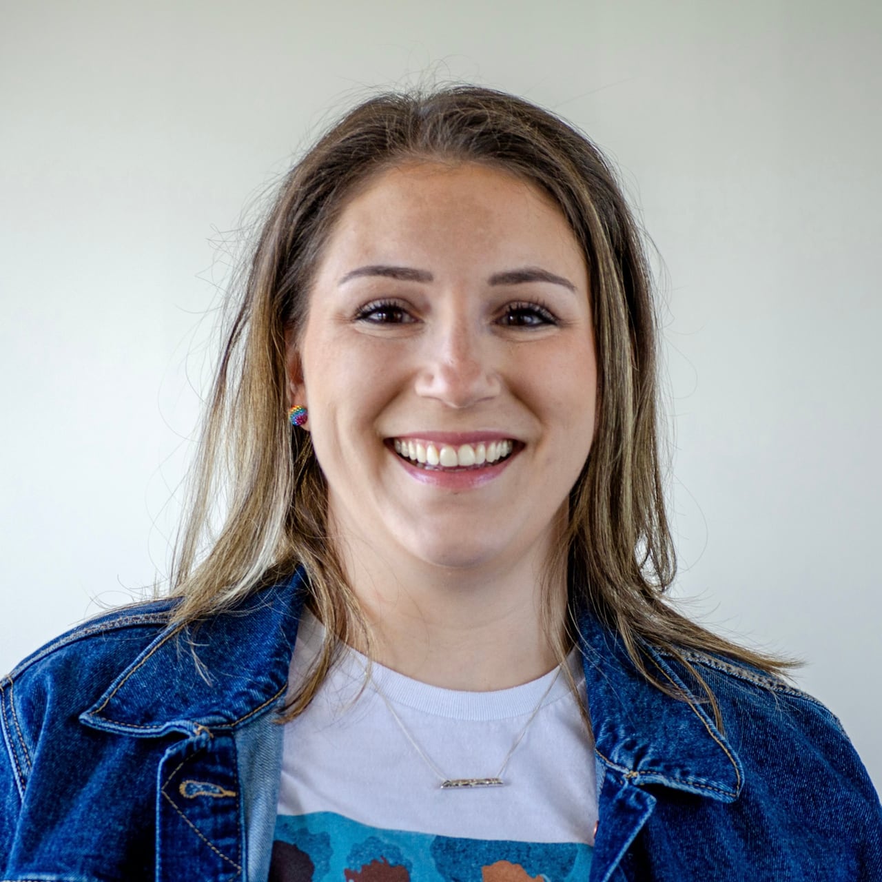 A smiling woman with straight, dark blonde hair is wearing a jean jacket and T-shirt
