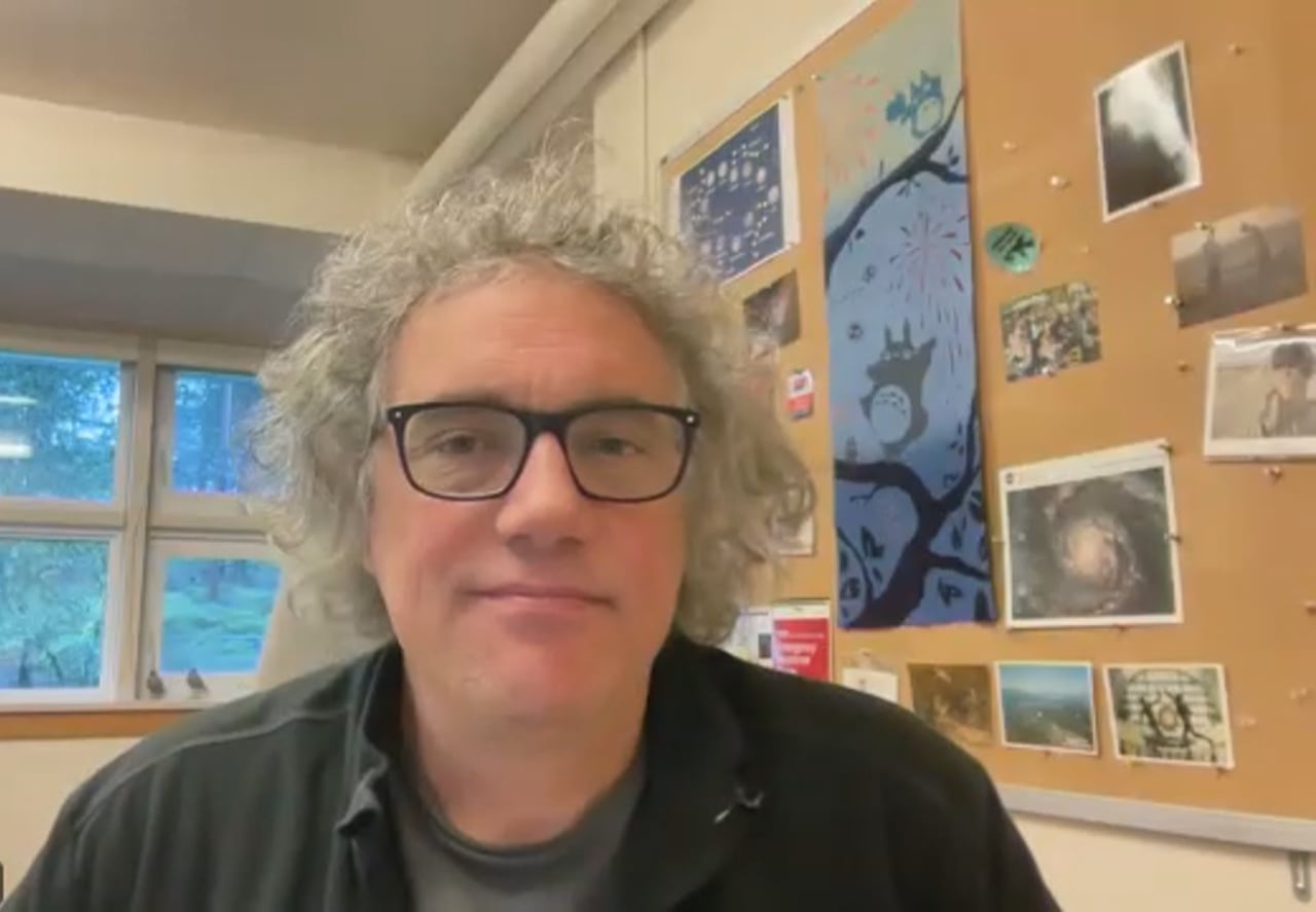 A man with white hair smiles in a Zoom screenshot.